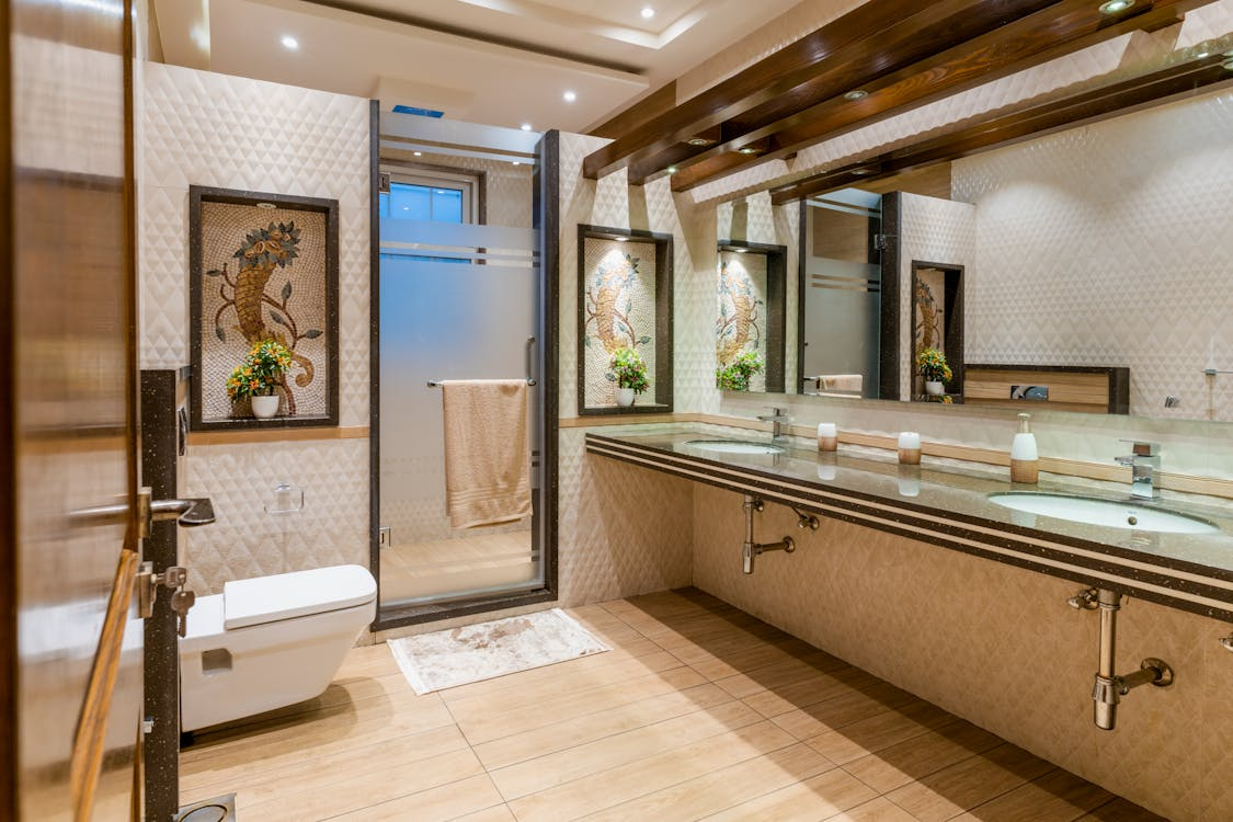 Luxury bathroom with double sink vanity, large wall mirrors, glass shower enclosure, and warm ambient lighting.