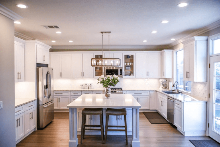 Modern white kitchen with large center island, quartz countertops, stainless steel appliances, and recessed lighting in a bright open-concept home.