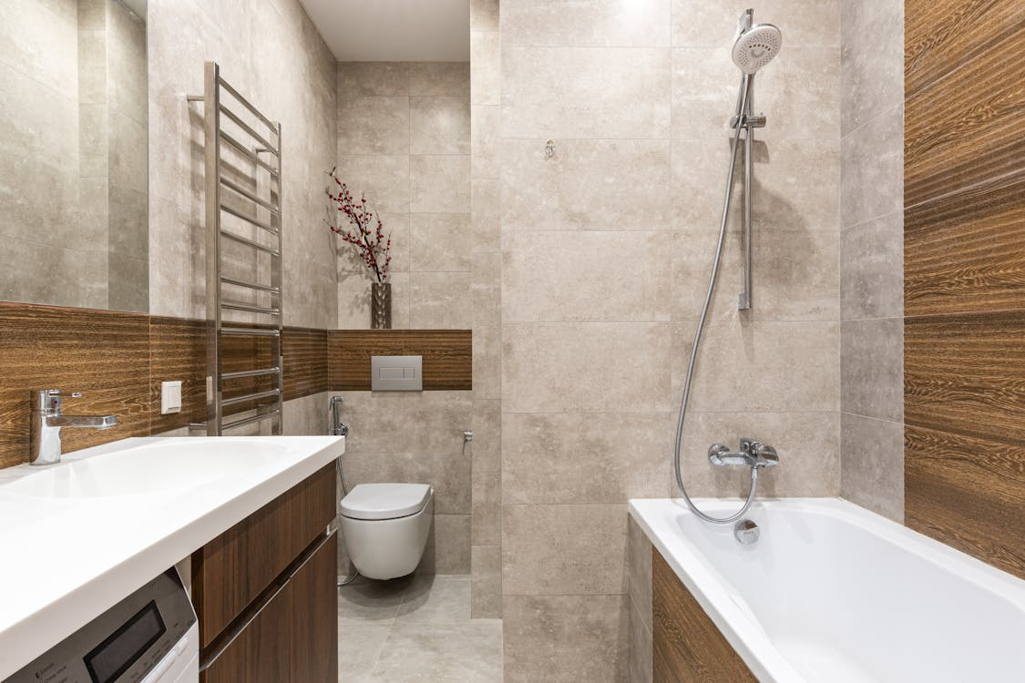 Modern bathroom with bathtub and shower combo, wood-accent wall panels, floating vanity, and large neutral stone tiles.